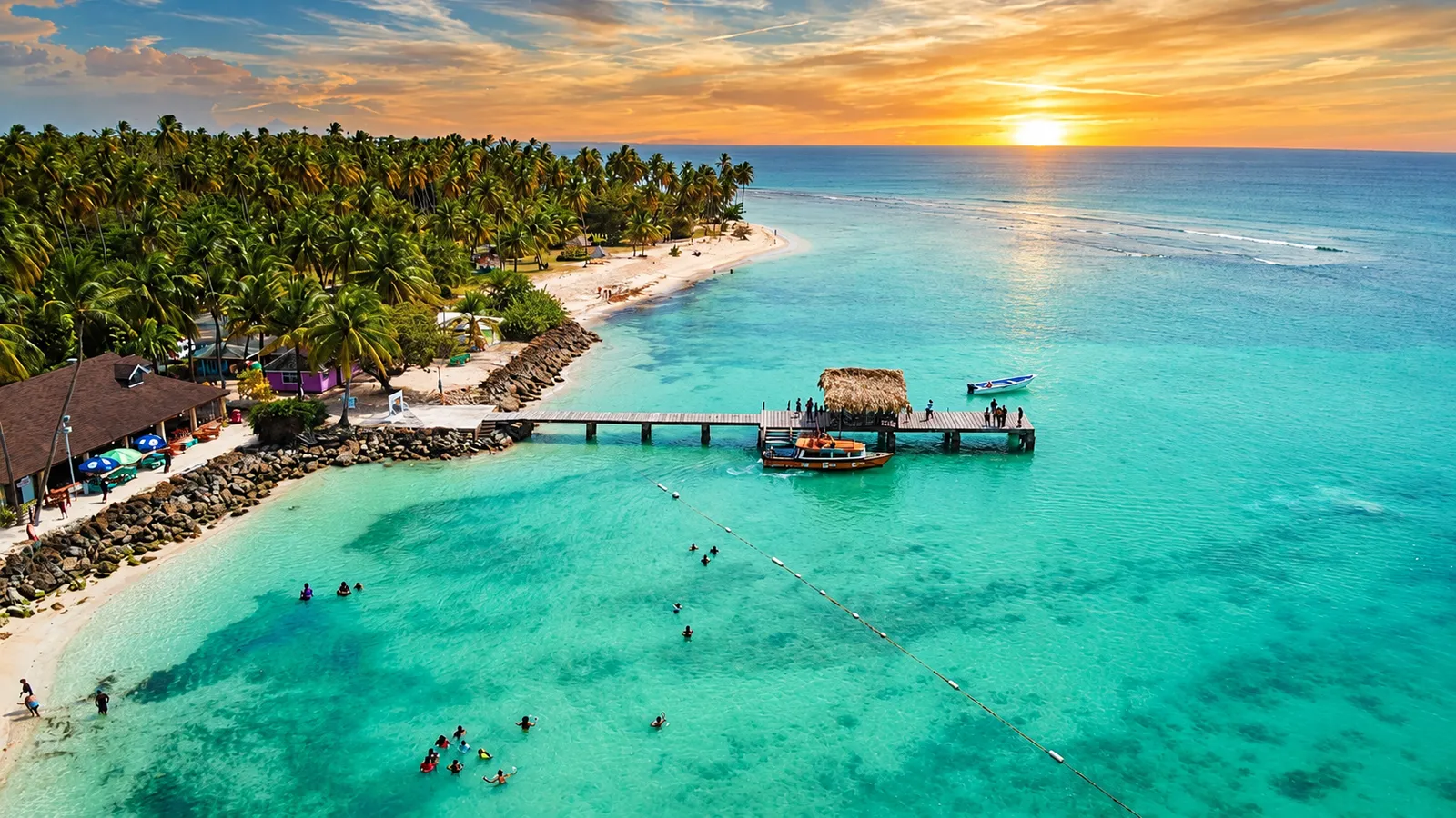 Swimmers in the shallows beside a wooden Andaman jetty at sunset