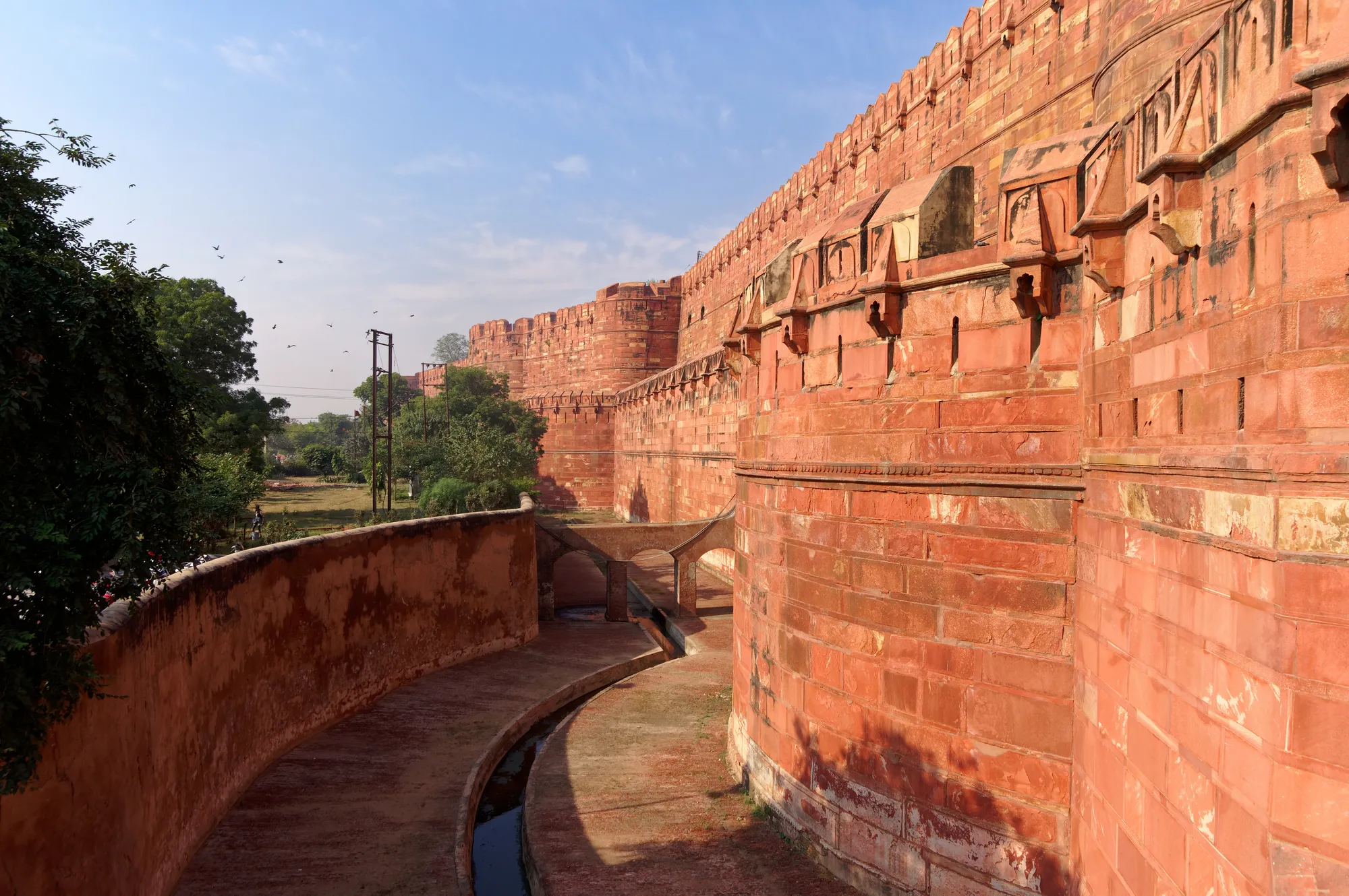 A curving red sandstone fortress wall above a dry moat