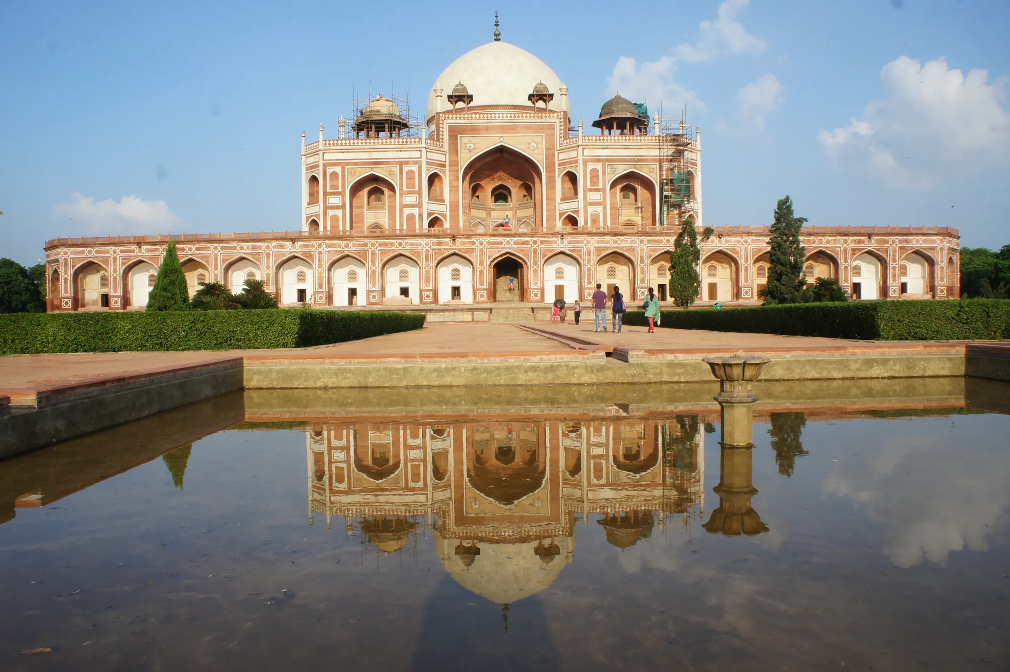 A red sandstone Mughal tomb reflected in a garden water channel