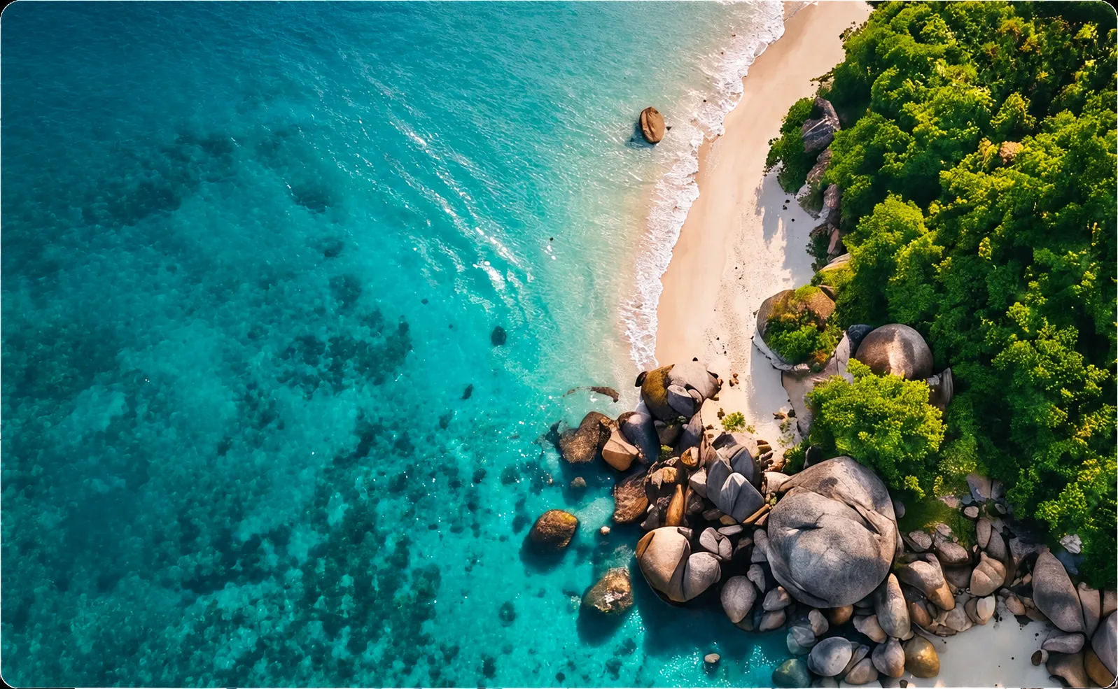 Turquoise shallows, pale sand and granite boulders along a forested Andaman shore, seen from the air