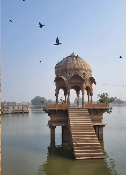 A stone pavilion standing in a still lake with steps leading down to it