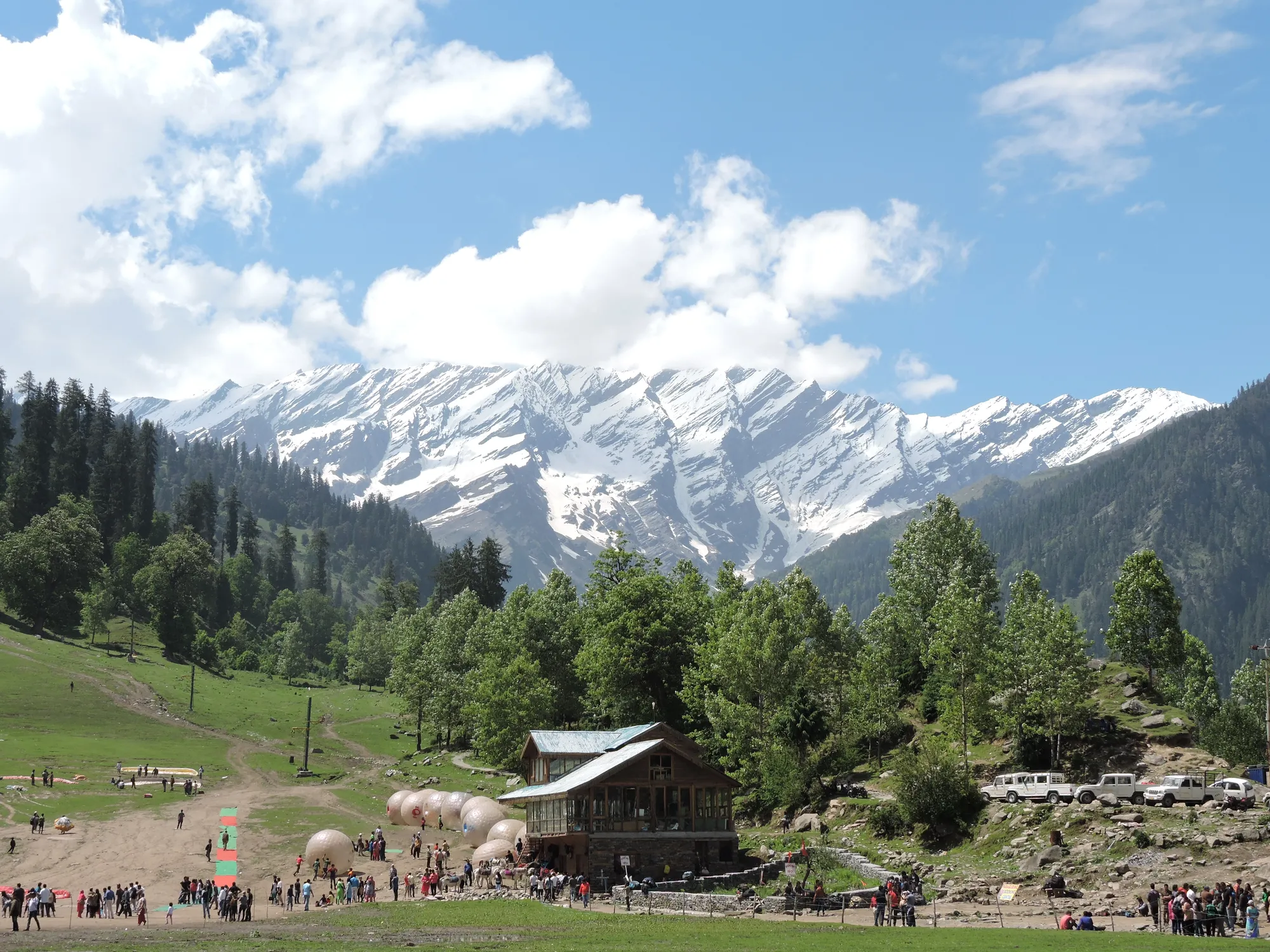 A green valley floor with huts below a snow-covered ridge