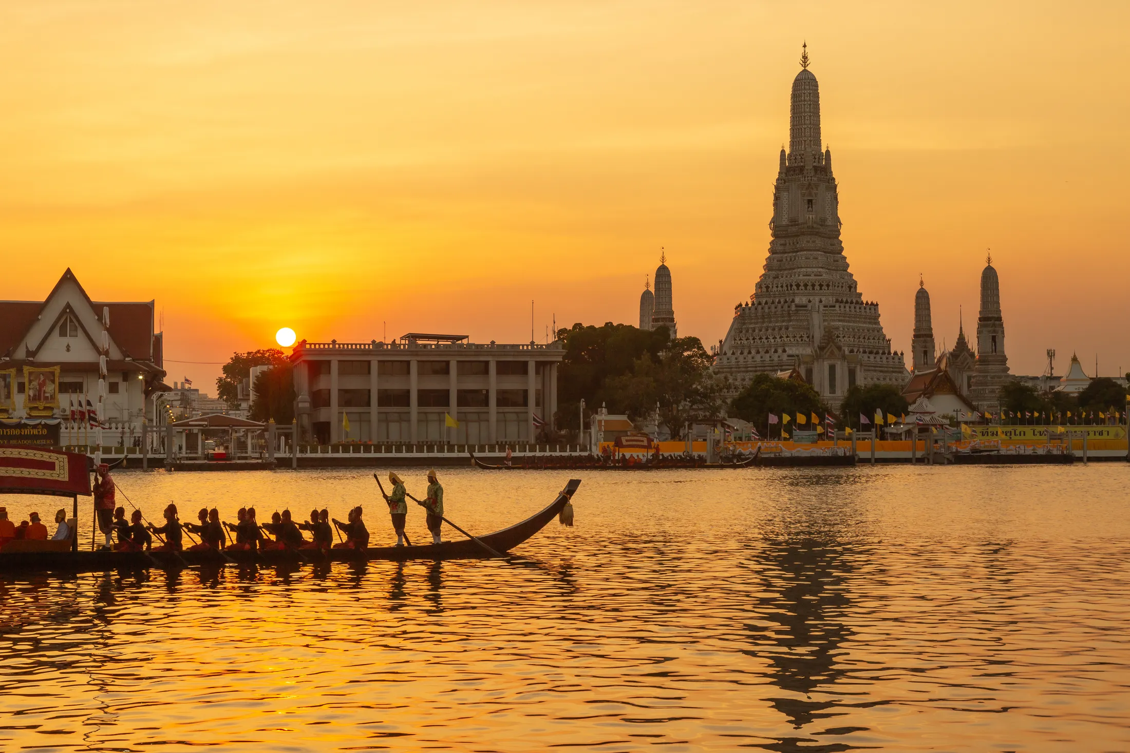 The prang of Wat Arun above the Chao Phraya at sunset, a royal barge crossing in front of it