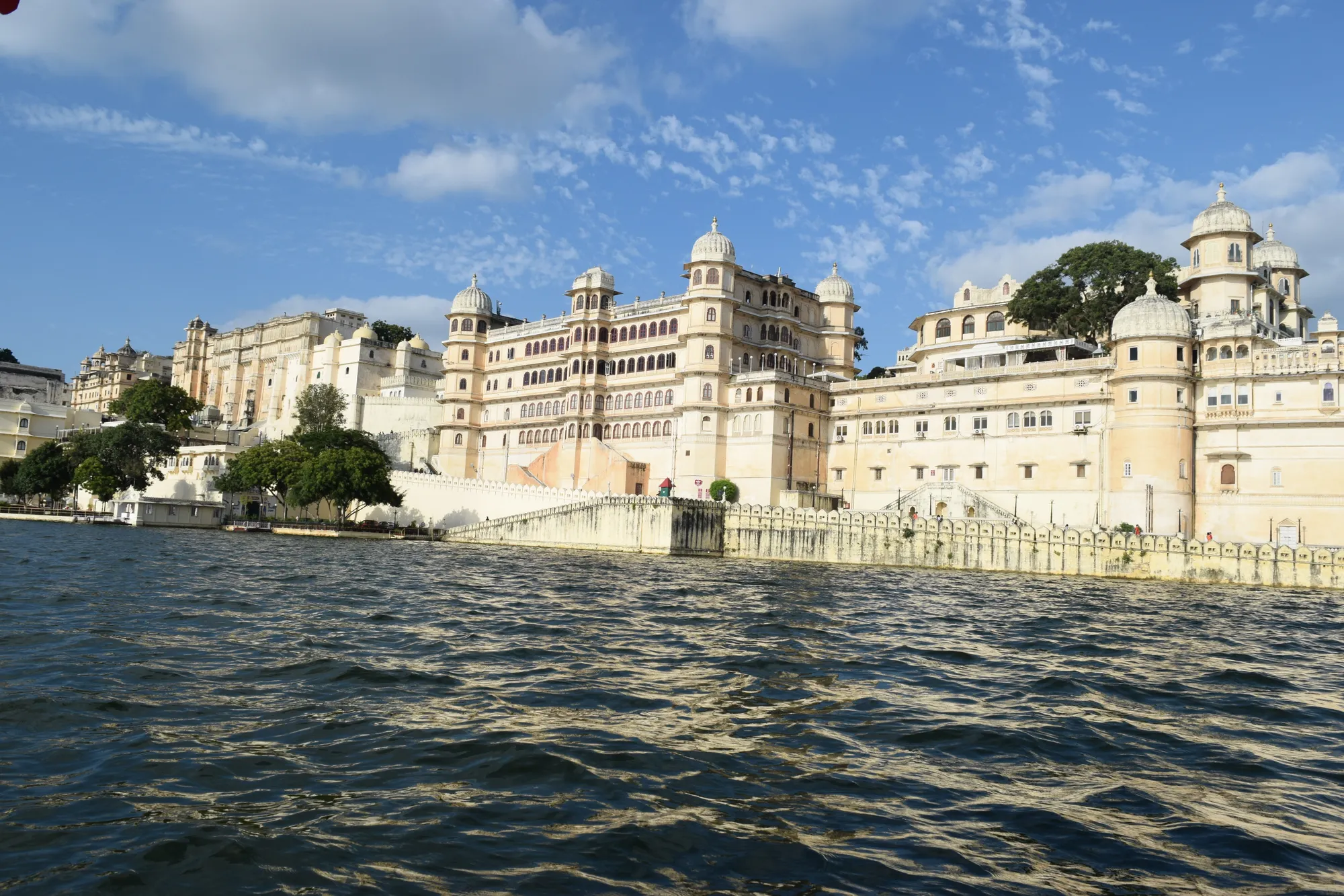 Palace buildings and ghats along a lake edge with boats below